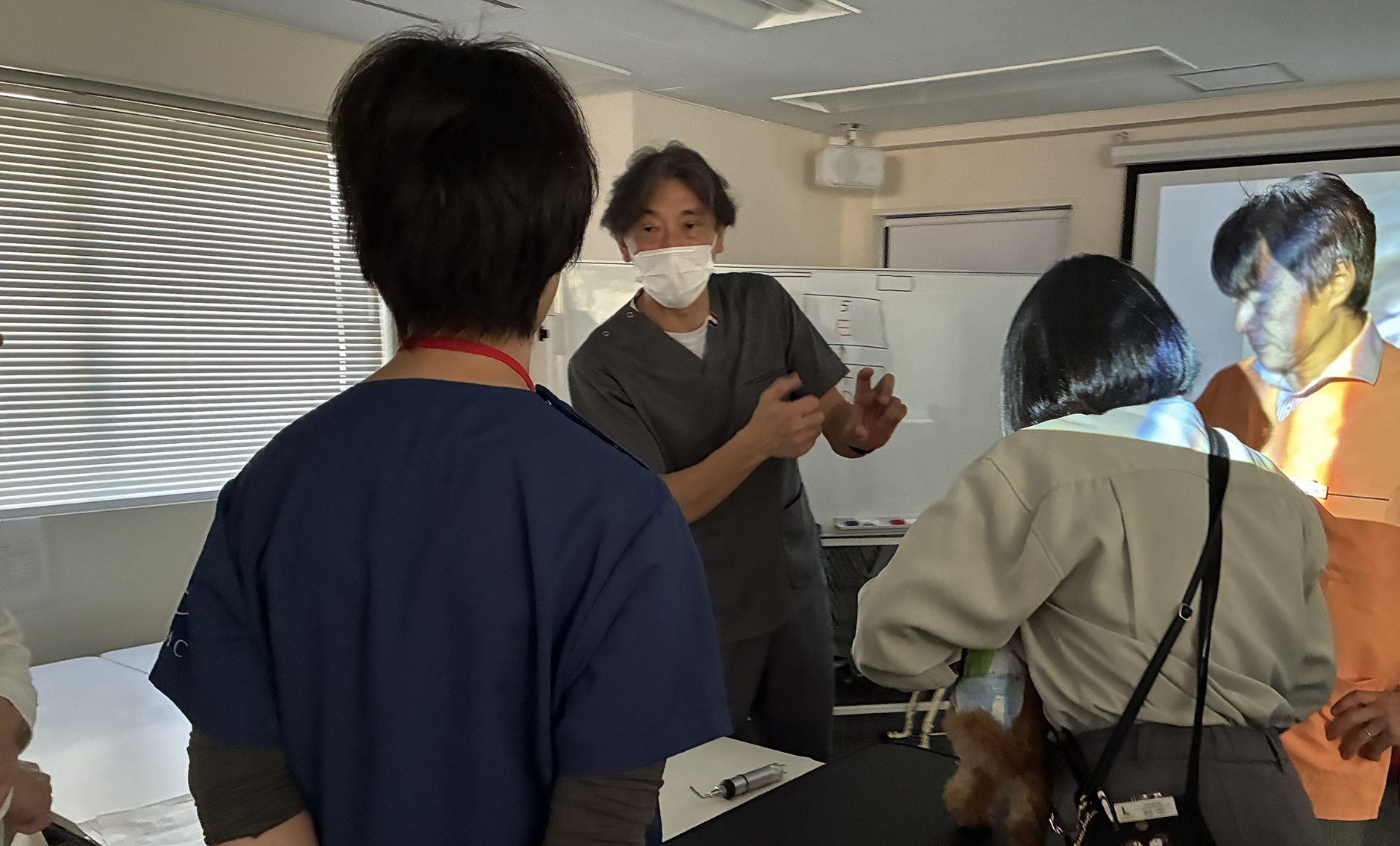 Life&Tailのスタッフに保定されている小さいプードル。その隣で参加者に説明をする小林先生と聞く参加者の方々